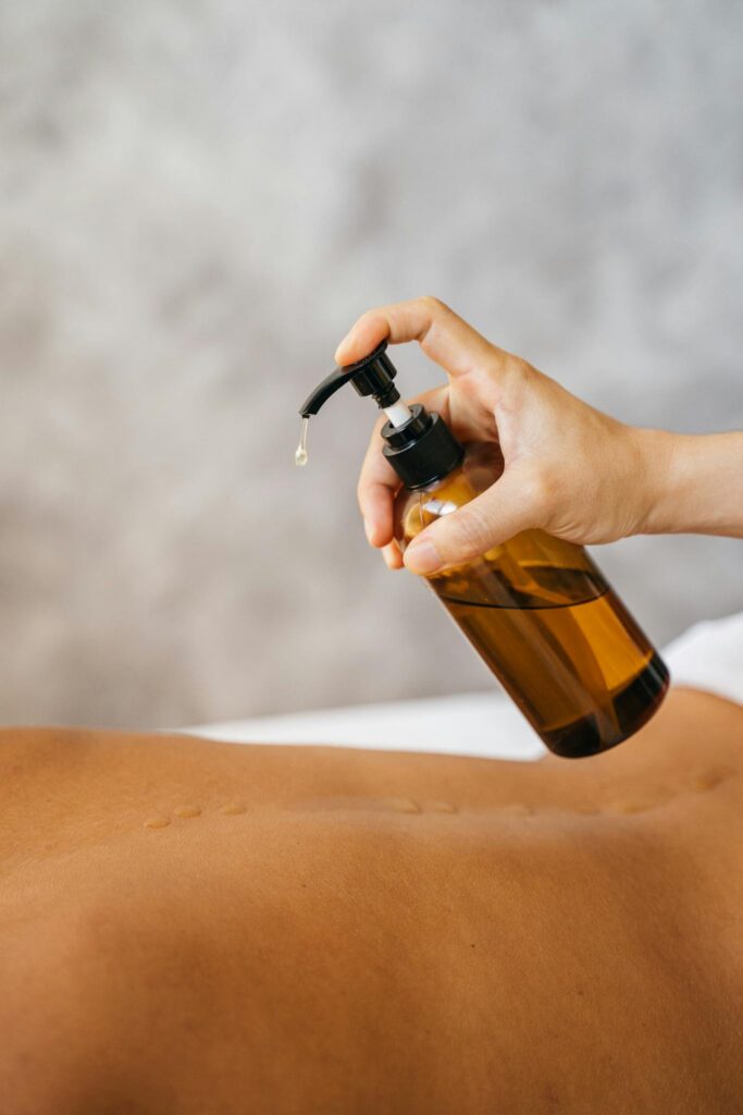 Hand holding pump bottle applying massage oil for relaxation and wellness.
