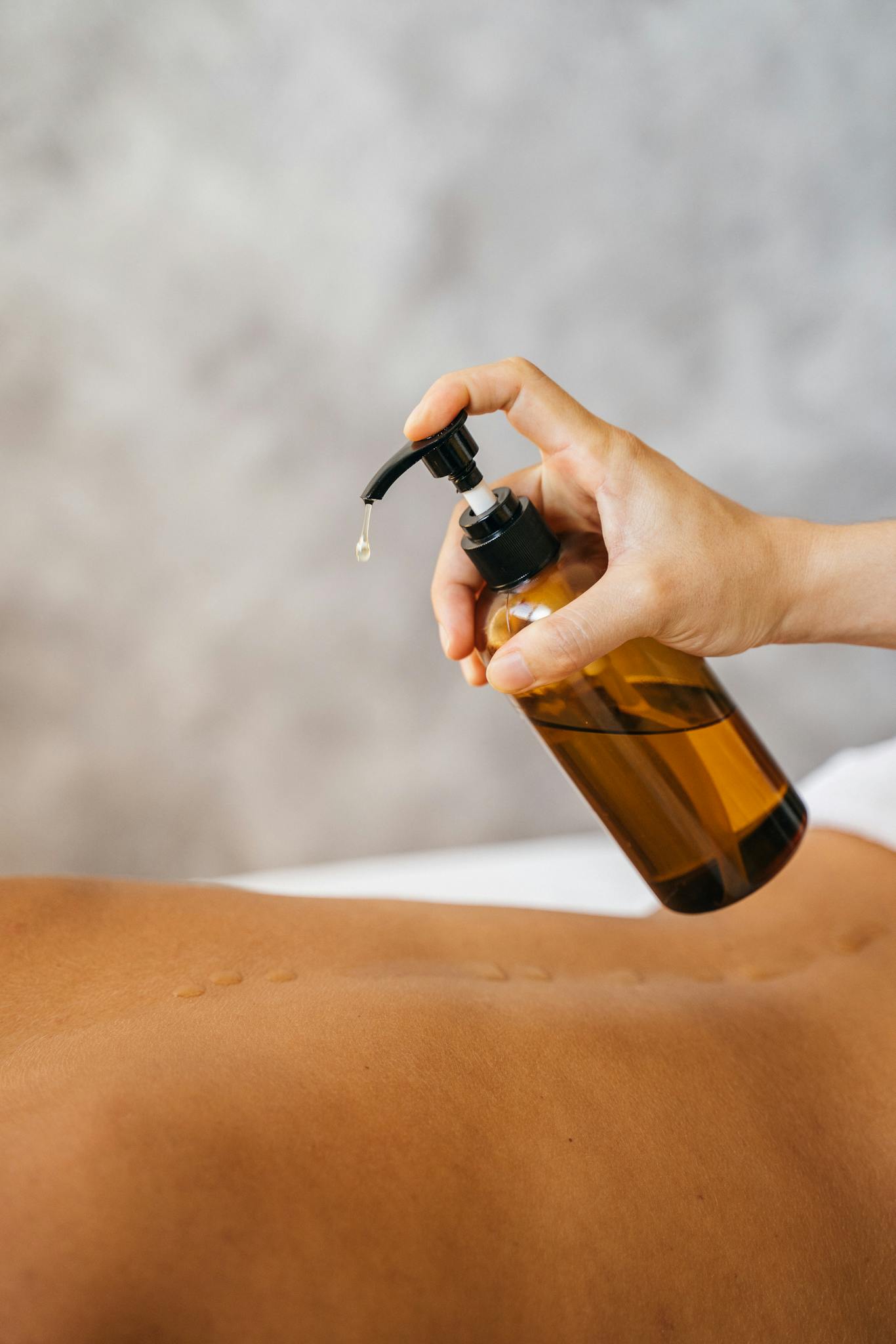 Hand holding pump bottle applying massage oil for relaxation and wellness.